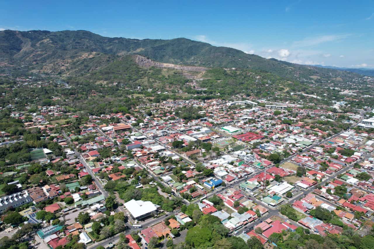 Vista de aceras renovadas y ciclovía en el centro urbano de Santa Ana con arborización y mobiliario urbano.